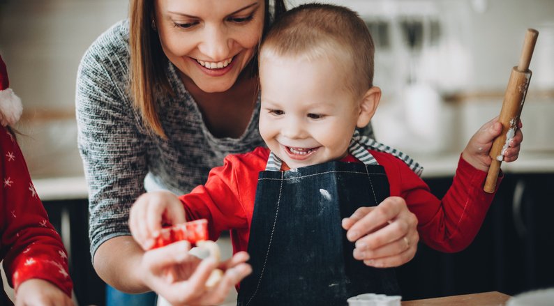 Parent and child laughing together while rolling out holiday cookie dough