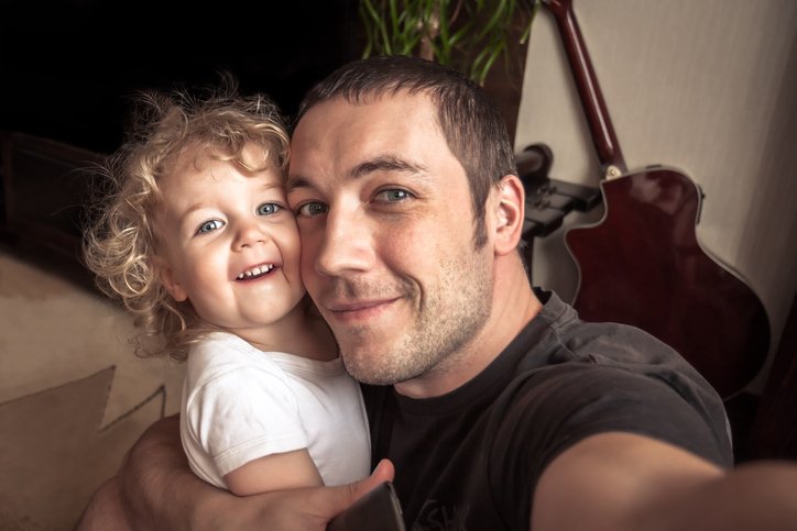 Parent and toddler laughing together while taking a selfie at home