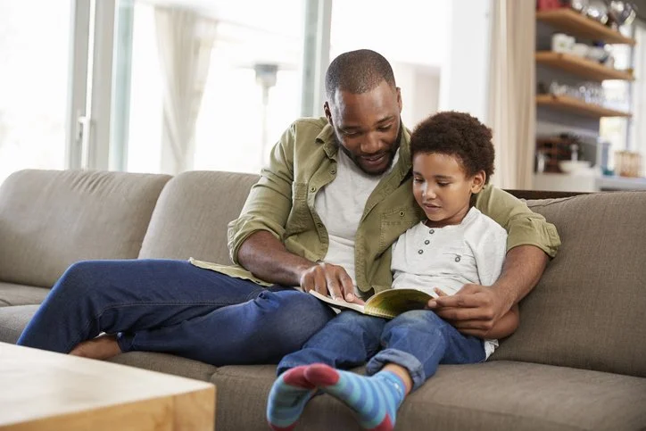Parent reading a book together with a child on the couch