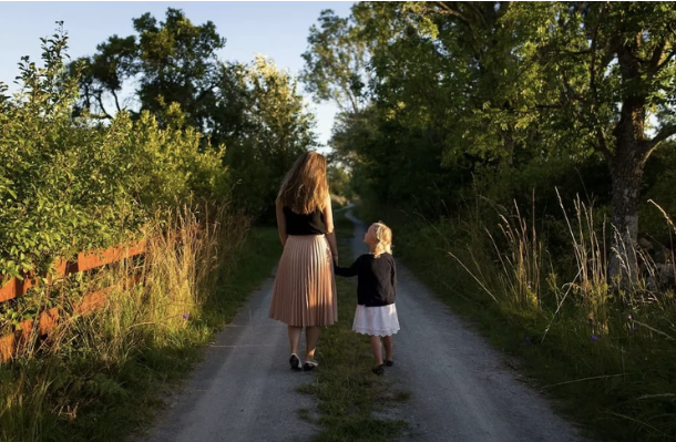 Parent and child walking hand in hand down a quiet country road