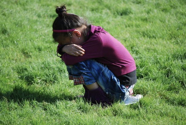 Older child kneeling to hug a younger child outdoors on the grass