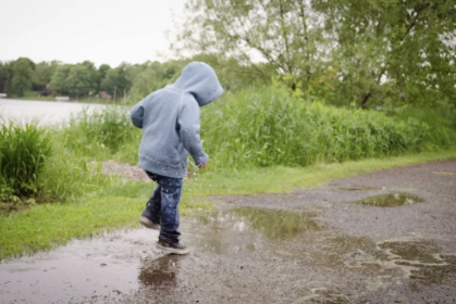 Child in a rain jacket jumping in a puddle along a path