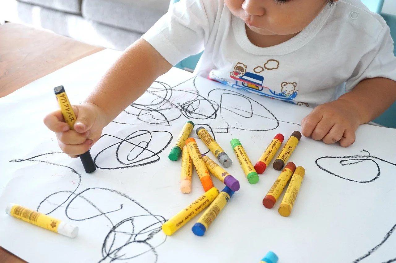 Child's hand drawing colorful scribbles with a handful of crayons
