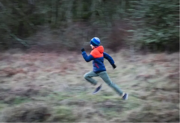Child running quickly through a wooded field wearing a helmet