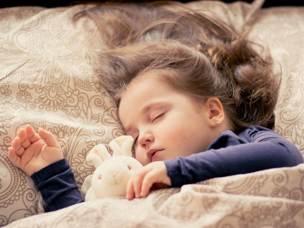 Young girl sleeping peacefully in bed with a stuffed bunny