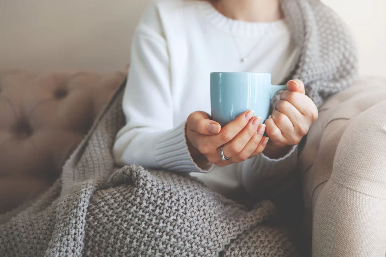 Person wrapped in a blanket holding a warm mug on the couch
