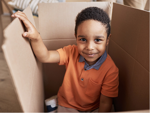 Young boy smiling while playing inside a cardboard box