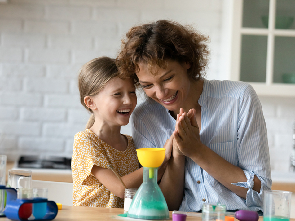 Parent and child laughing together while mixing colors in an at-home science experiment