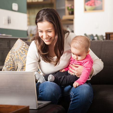 Parent and baby looking at a laptop screen together on the couch