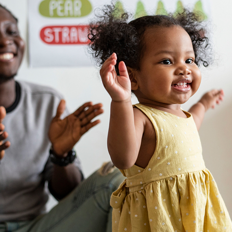 Toddler dancing joyfully while a caregiver claps nearby in a classroom