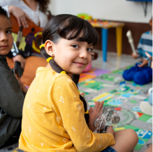 Child smiling over their shoulder in a classroom while other children play nearby